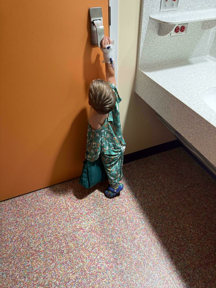 A small child in hospital attire reaching for a door handle, captured in wholesome pics of dads supporting their children