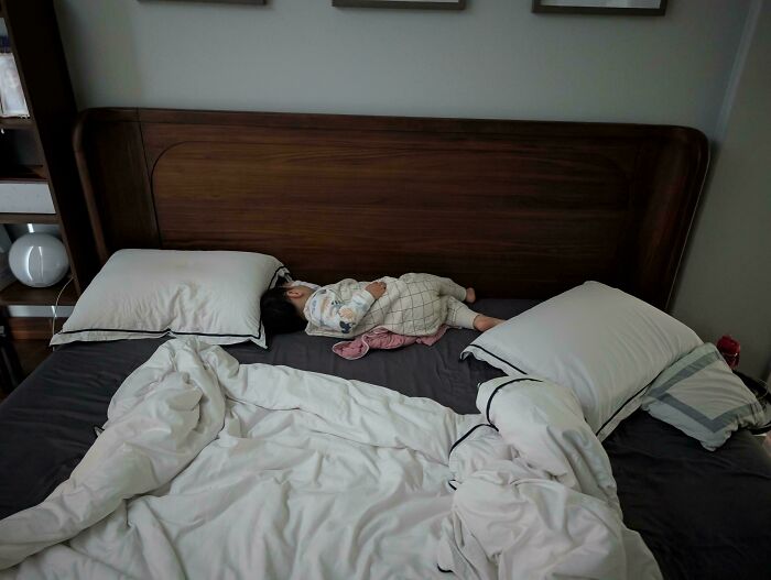 A toddler sleeping on a large wooden bed, representing wholesome pics of dads capturing cozy family moments