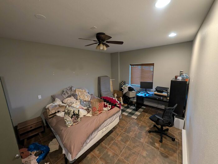 A bedroom with an unmade bed, bags, and a home office desk setup for wholesome dad life.