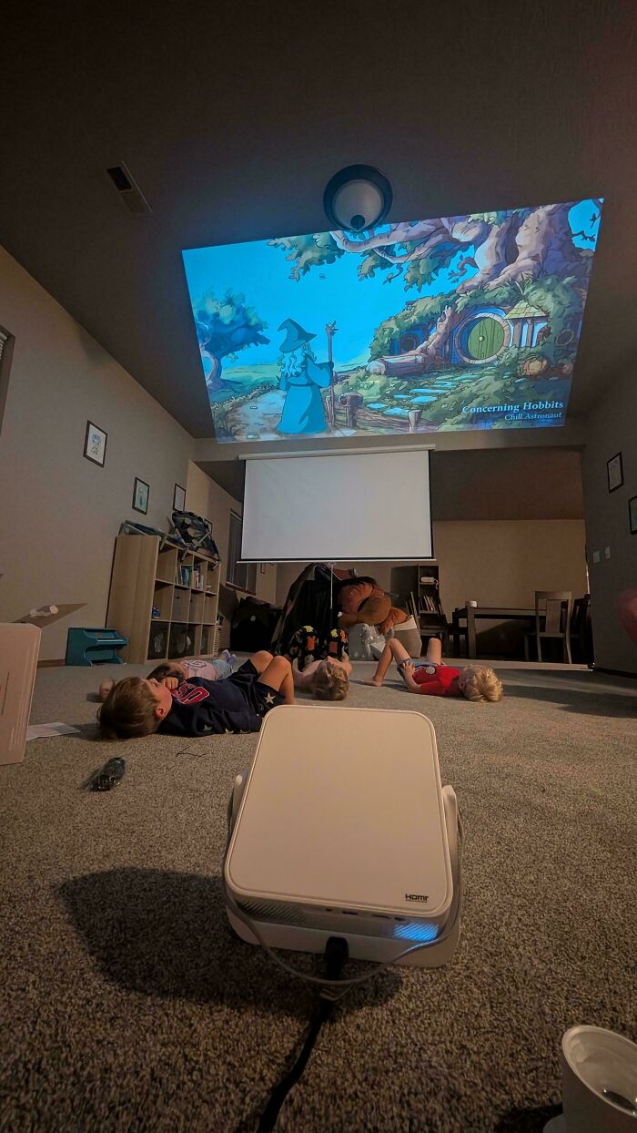 Children lying on the carpet watching a projected movie ceiling display during a fatherhood activity.