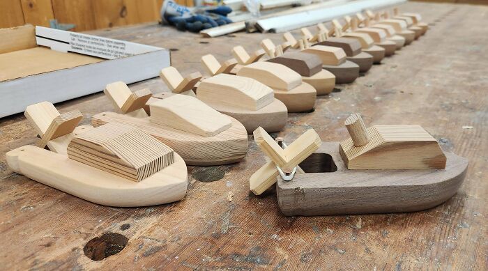 Row of handcrafted wooden toy boats neatly arranged on a wooden workbench.
