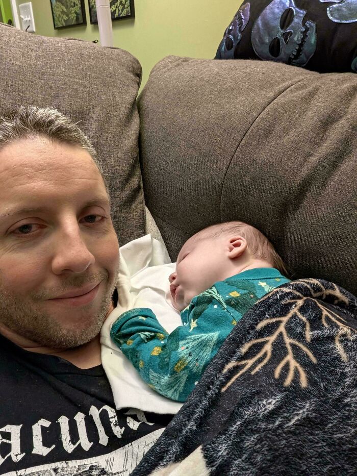 A father resting peacefully on a sofa while his newborn baby sleeps soundly on his chest.