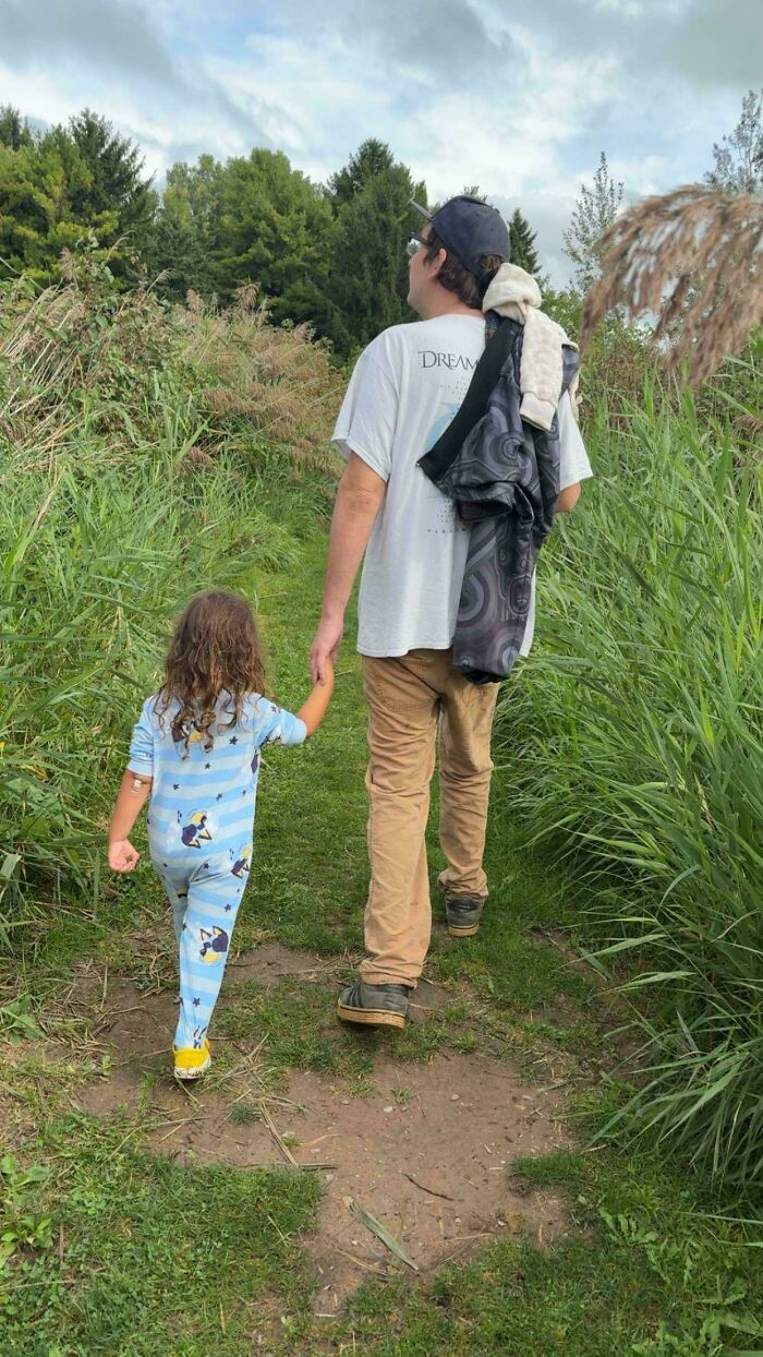 Dad holding hands with his young child walking along a grassy nature path, showing wholesome pics of dads.