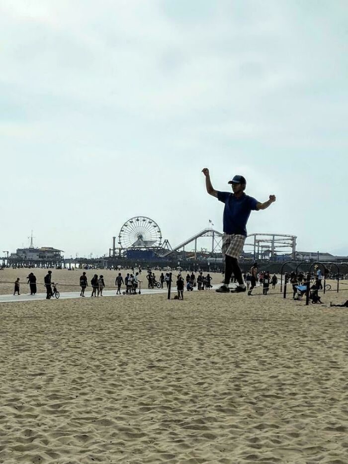 Man walking on slackline above sand at beach with amusement park in background