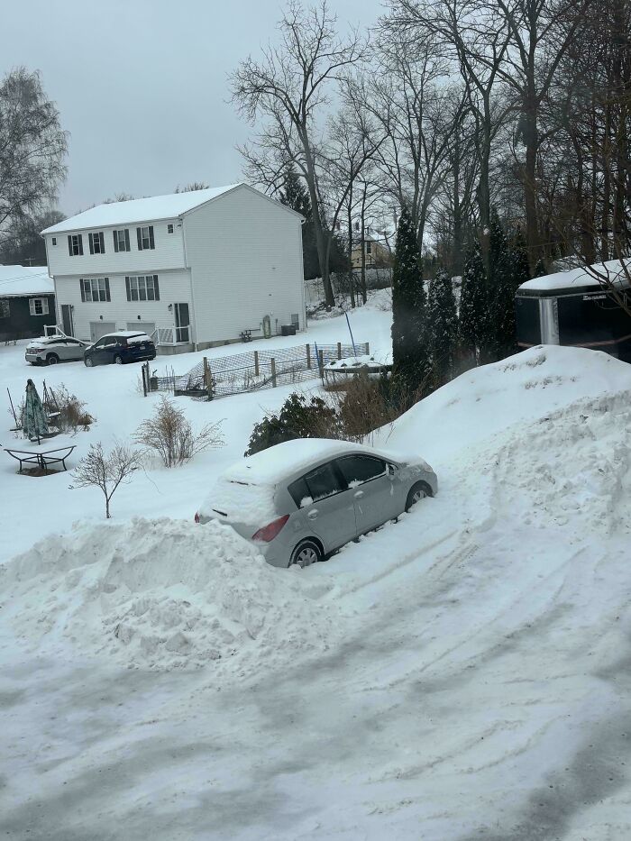 A car buried in snow plowed by a landlord in an apartment complex parking lot