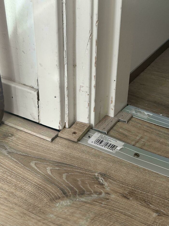 Poorly installed flooring transition strip with cardboard and adhesive, highlighting a terrible landlord fix.