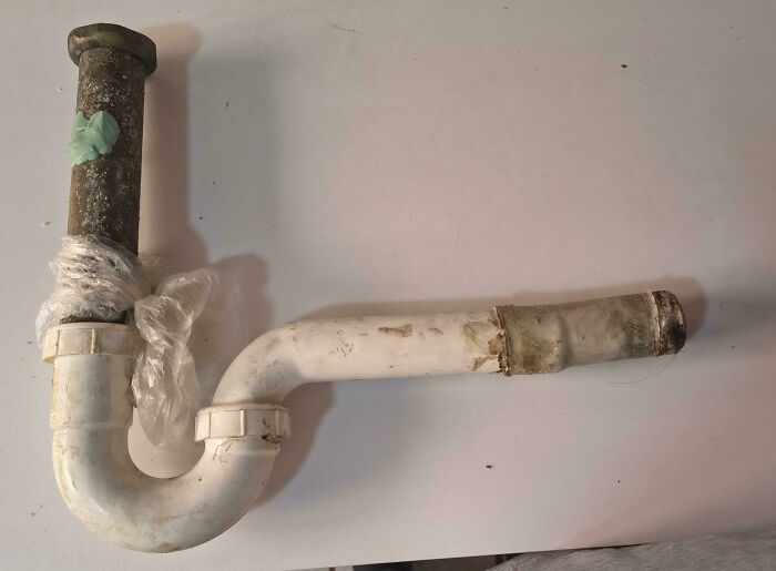 A dirty sink pipe held together with plastic wrap and tape, demonstrating terrible landlord plumbing.