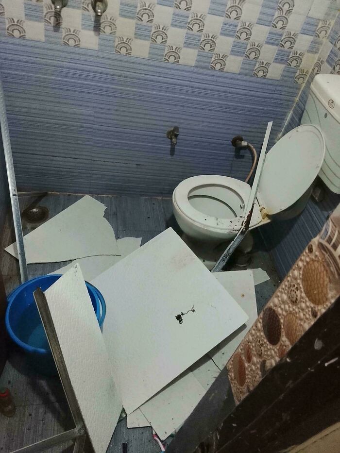 A messy bathroom floor covered in broken ceiling tiles, showcasing terrible landlord maintenance neglect.