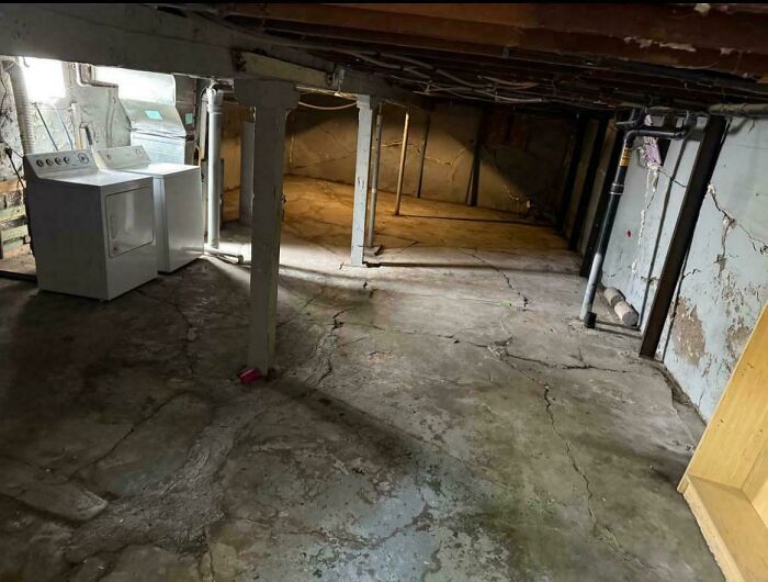 An unfinished basement laundry room with cracked concrete floor, showing terrible landlord conditions