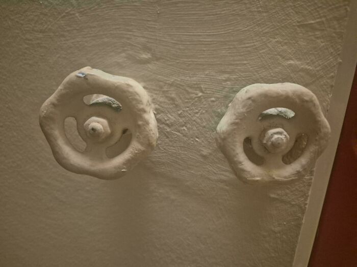 Two white faucet knobs heavily covered in white paint, showcasing a terrible landlord repair job.