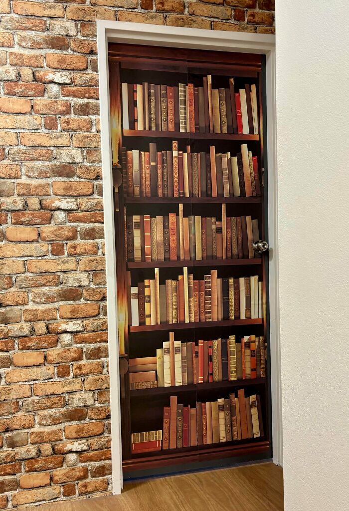 A door with a realistic bookshelf decal set into a rustic brick patterned wall.