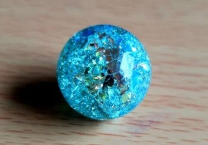 A vibrant blue cracked glass marble sitting on a wooden surface, displaying cool photos of everyday objects