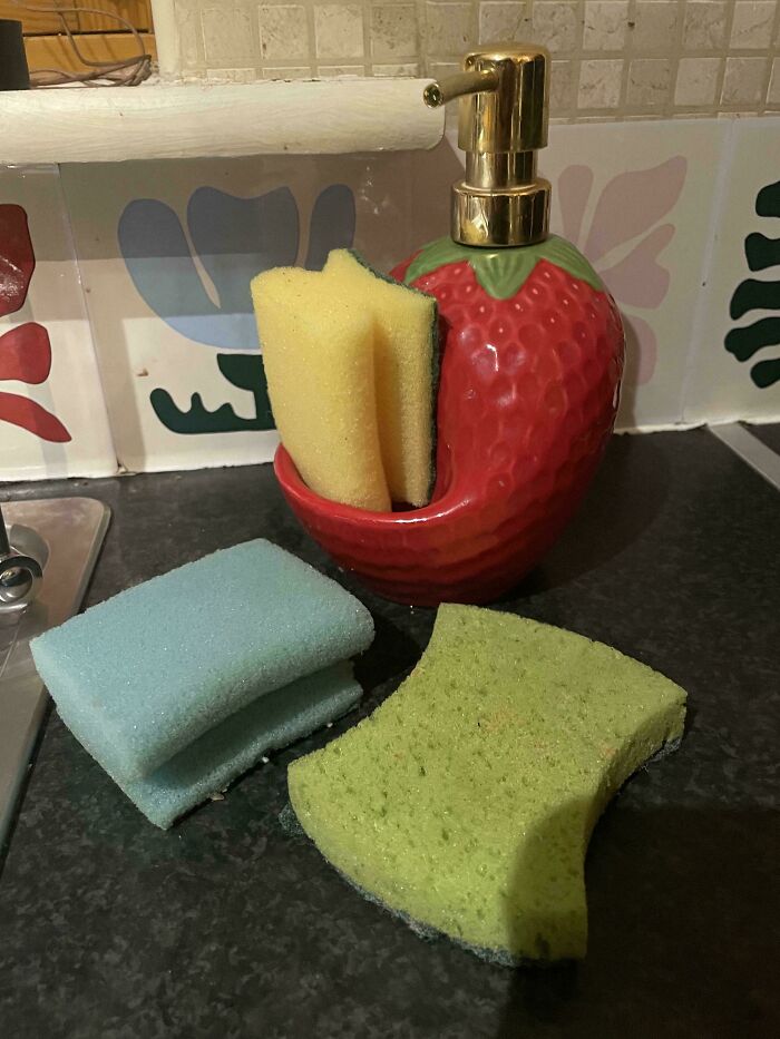 Strawberry-shaped soap dispenser holding sponges, with more kitchen sponges scattered around it.