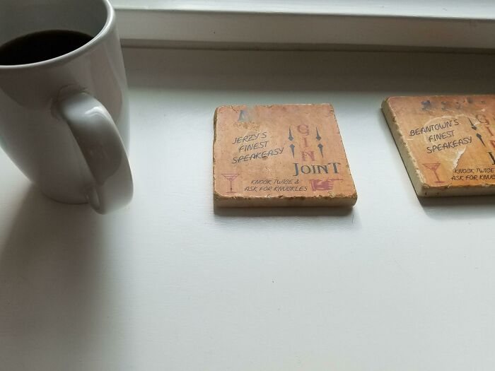 A white coffee mug sits next to vintage-style coasters on a white windowsill.