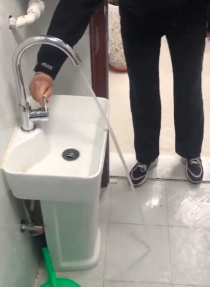 Poorly placed faucet spraying water onto the floor from a small bathroom pedestal sink.