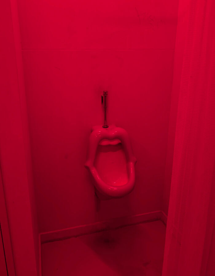 A lip-shaped red urinal mounted on a wall under red lighting, an example of awful creations in design.