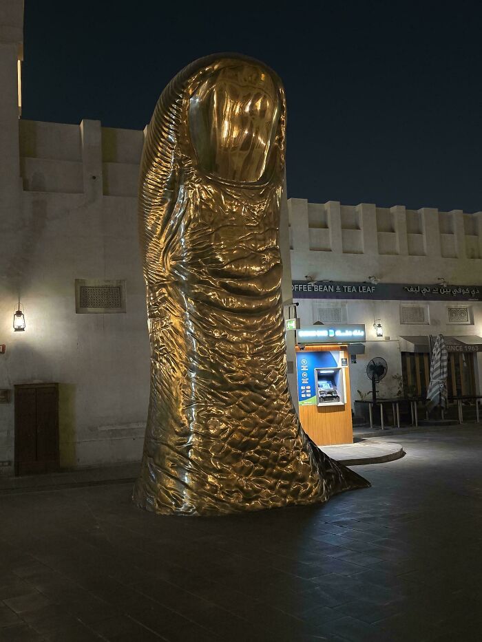 Awful creations featuring a giant bronze sculpture of a thumb standing in a city square at night.