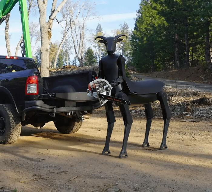 Black centaur robot holding a chainsaw by a pickup truck, an awful creation far too well-made to ignore.