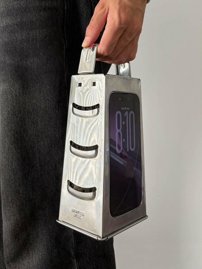 Hand holding a phone inside a metal grater, an awful creation far too well-made to ignore.