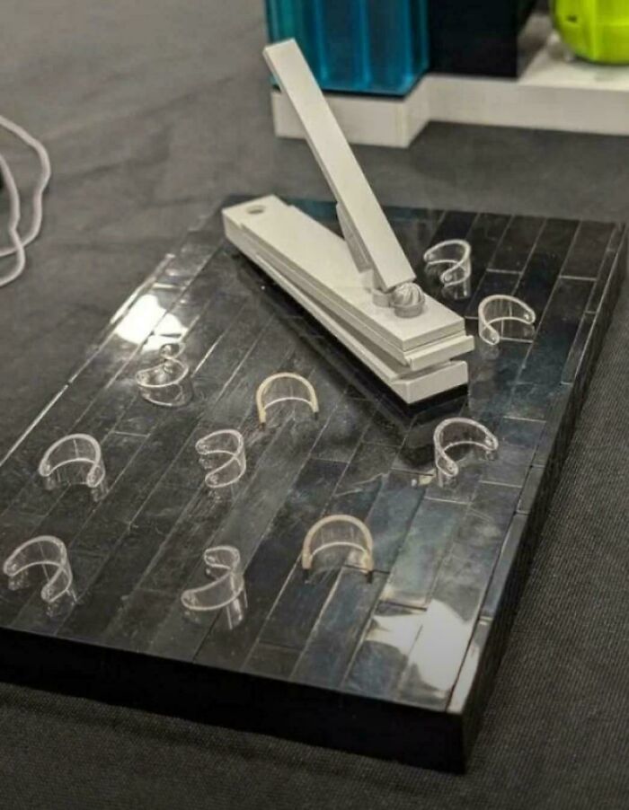 Realistic glass or metal sculpture of a giant nail clipper holding false nails among creations awful to look at.