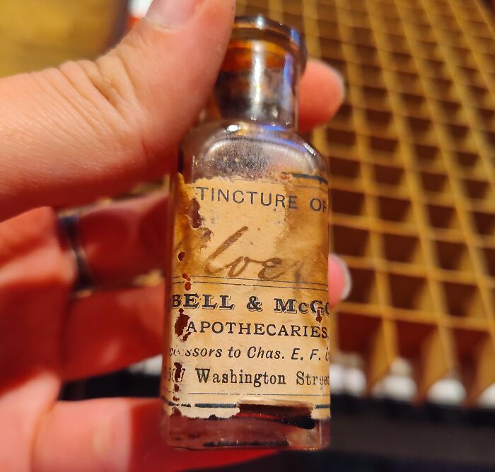 A hand holding an antique apothecary glass bottle of Tincture of Clove from medical history.