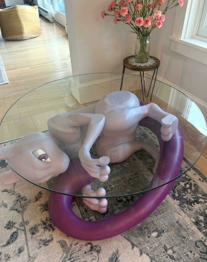 Glass coffee table supported by a Mewtwo sculpture, one of many creations awful to look at.