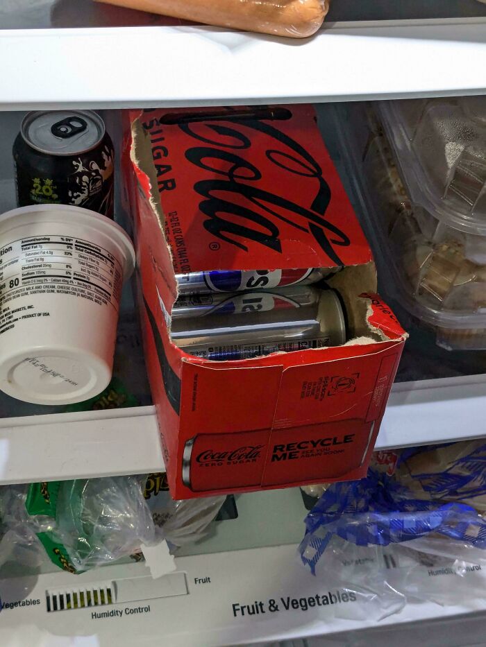 A cardboard box of soda cans opened incorrectly inside a refrigerator