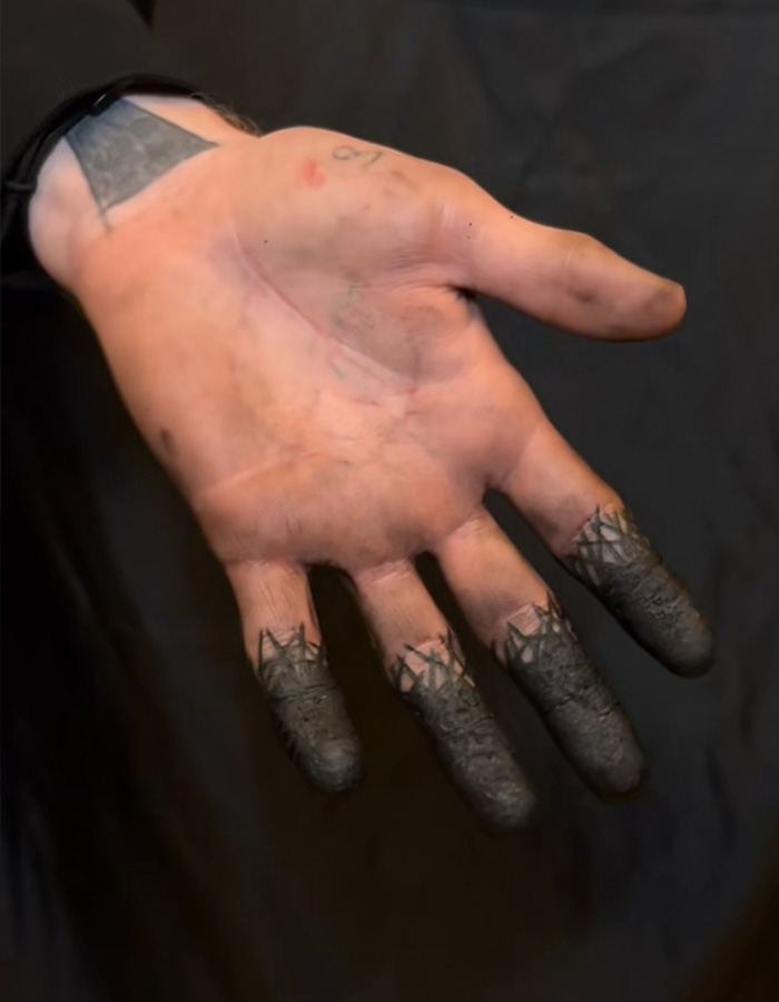 A palm showing a solid black fingertip tattoo design with sharp jagged edges on the fingers. A palm showing a solid black fingertip tattoo design with sharp jagged edges on the fingers.