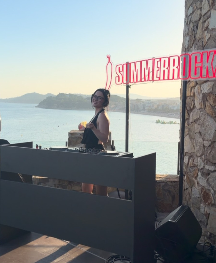 The 'Red Bikini Girl' DJing outdoors, overlooking the ocean, revealing her income on the adult platform. The 'Red Bikini Girl' DJing outdoors, overlooking the ocean, revealing her income on the adult platform.