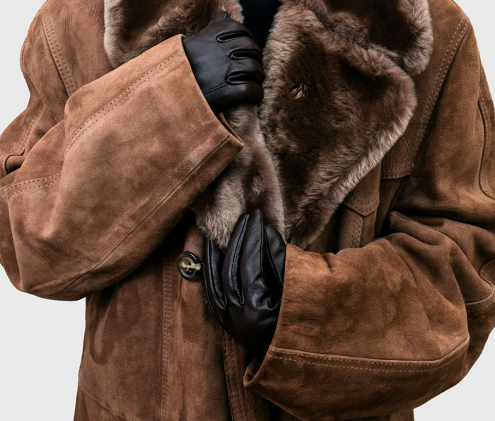 A person wearing a warm brown fur-lined coat and black gloves, symbolizing warmth and stories of karma
