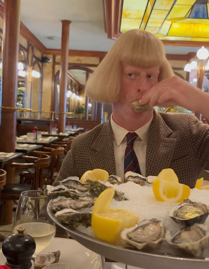 A mysterious influencer with a blond bob haircut eats oysters at a restaurant table
