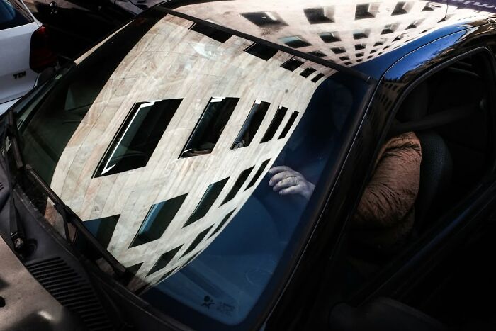 A street photographer captures an odd coincidence: a building reflection perfectly aligned on a car's windshield.