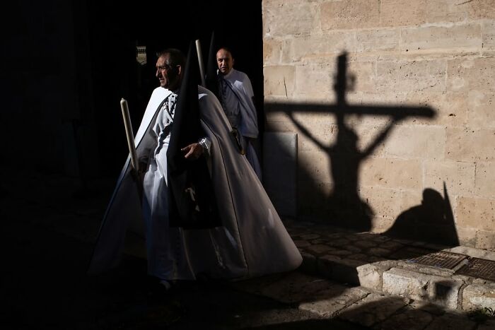 A street photographer capturing an odd coincidence: a man in a white cloak with a cross shadow on the wall.
