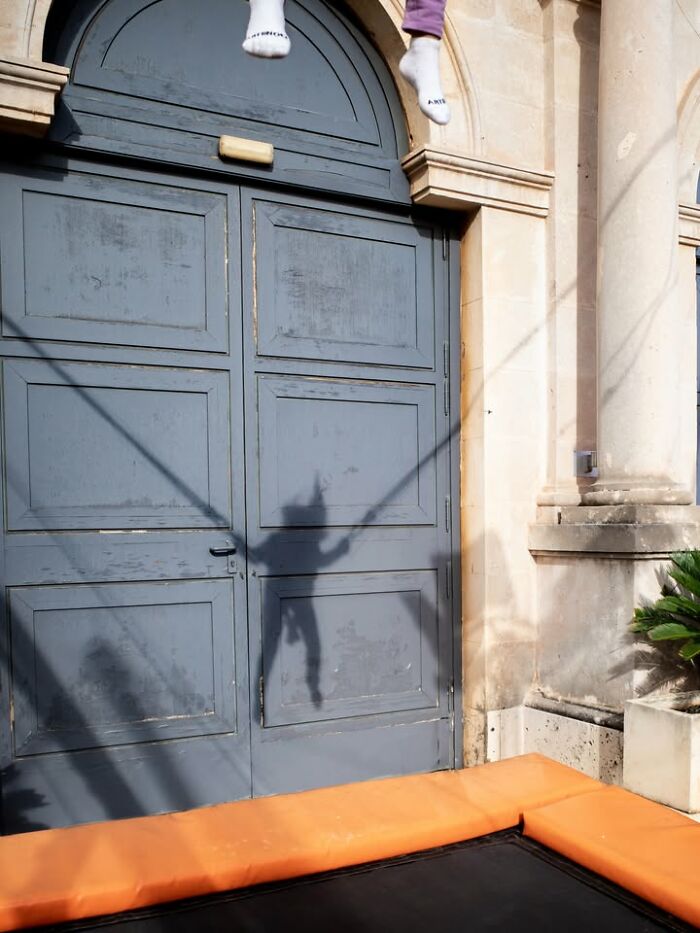 A street photographer captures a shadow of someone jumping on a trampoline, an odd coincidence on the street.
