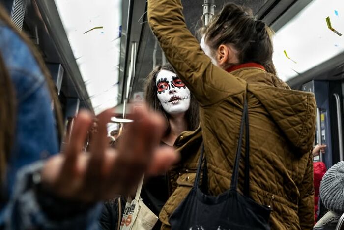 A street photographer captures a person with skull face paint on a train, an odd coincidence.