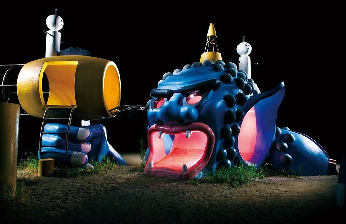A vibrant blue monster playground with an open mouth slide at night, part of the surreal Japanese playgrounds.