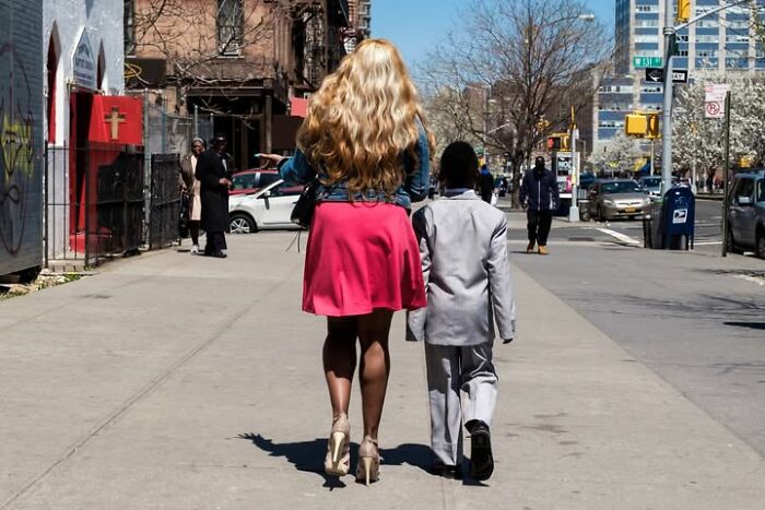 A street photographer captures a tall woman in a pink skirt and a small person in a grey suit walking.