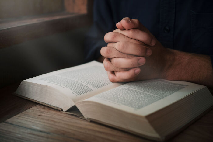 Hands clasped in prayer over an open book, symbolizing introspection on ways people ruin their lives.