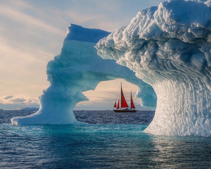 A sailboat with red sails glides through an ice arch, representing remarkable places and people.