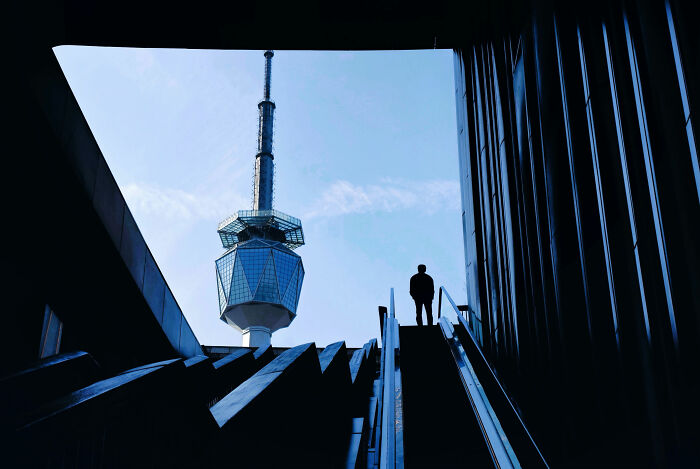 Bold minimalist architecture photography features a man on stairs framed by modern buildings and a tower.