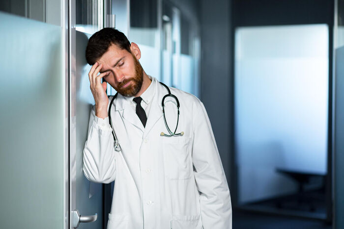 A tired doctor leaning on a wall in a hospital, depicting the stress associated with standard medical procedures.
