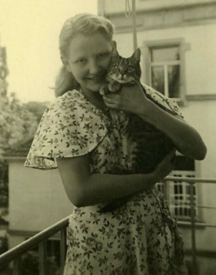 A smiling young woman holding her tabby cat on a balcony, showing felines in vintage cat photos.