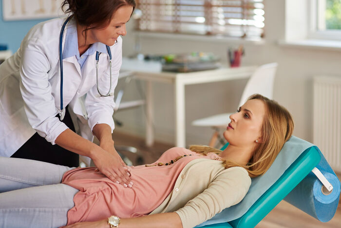 A doctor performs a medical procedure, palpating the abdomen of a female patient lying on an examination table.