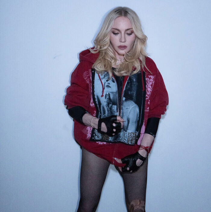 Madonna wearing red hoodie and fishnet stockings posing against a plain wall Madonna wearing red hoodie and fishnet stockings posing against a plain wall
