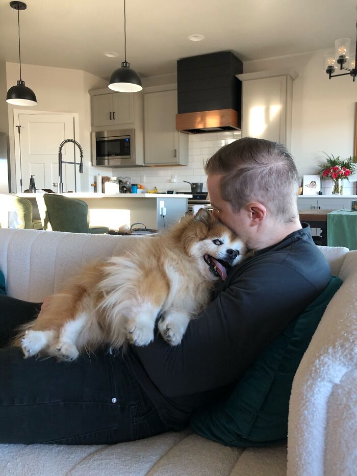 A man cuddles his fluffy dog on the couch, showing proof of the right man and sweet companionship.