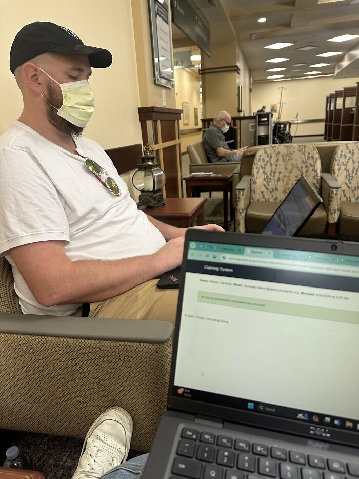 A man wearing a mask and working on a laptop in a waiting room, proof of finding the right man.