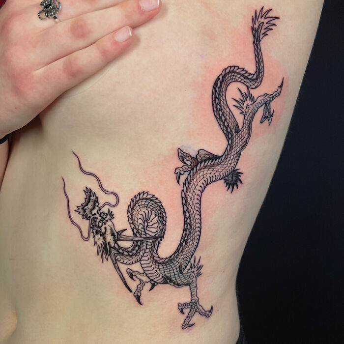 Stunning mythology tattoo of a delicate dragon on a womans side, from Sacred Gold Studio.