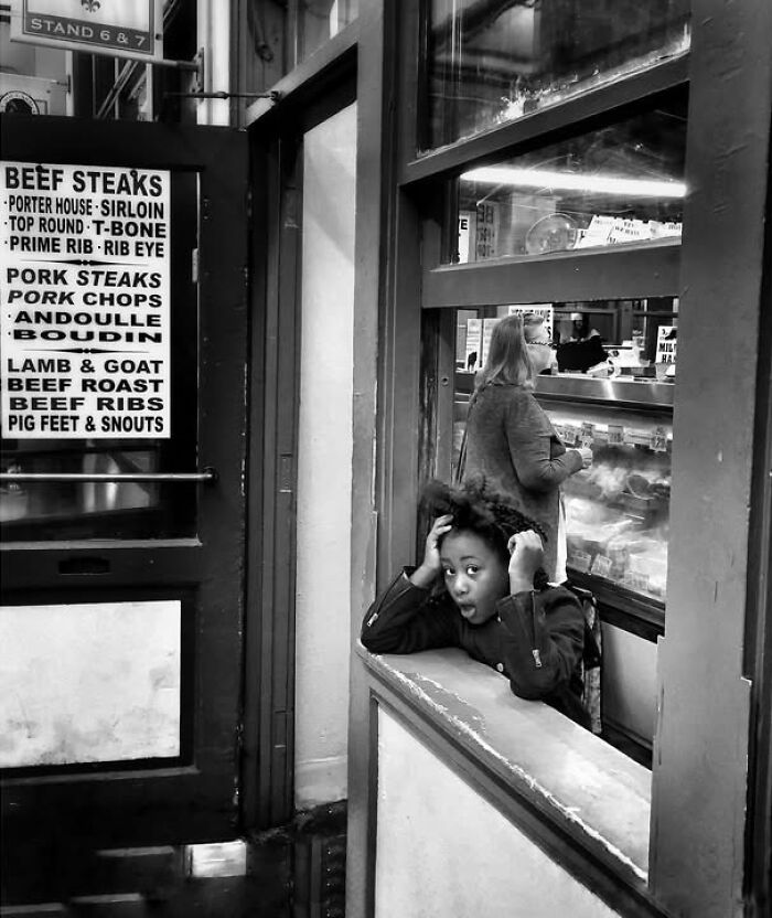 A captivating street photo by Taylor Coble showing a child with a surprised expression looking out a window, next to a menu.