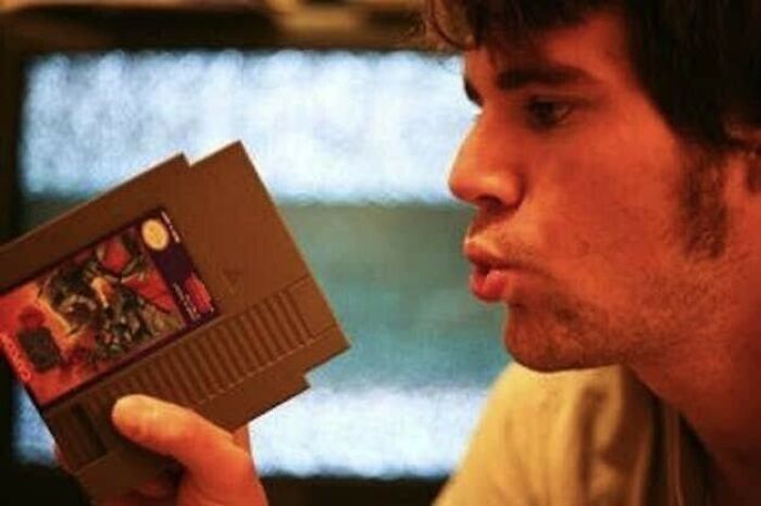 A person blowing into a retro video game cartridge, a common practice for 80s tech gamers.