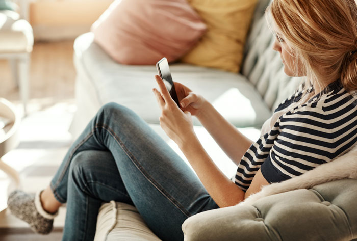 A woman relaxing on a sofa, looking at her phone, possibly reading stories of women doing crazy things for a crush.